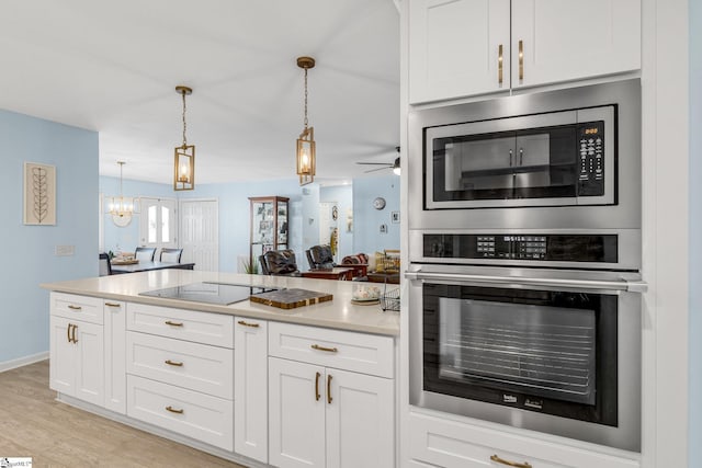 kitchen with white cabinetry, stainless steel appliances, decorative light fixtures, and light hardwood / wood-style floors