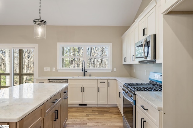 kitchen featuring appliances with stainless steel finishes, white cabinets, a sink, and light stone countertops