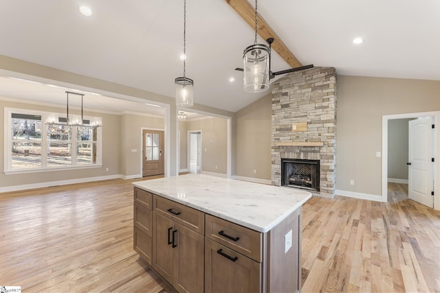 kitchen with open floor plan, a center island, vaulted ceiling with beams, a stone fireplace, and pendant lighting