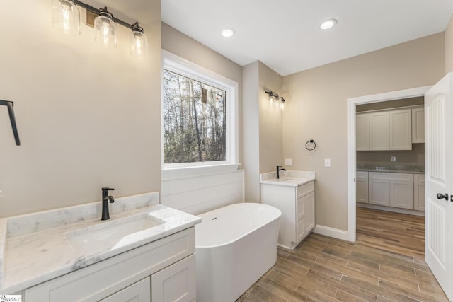 bathroom featuring recessed lighting, wood finished floors, two vanities, a sink, and a soaking tub