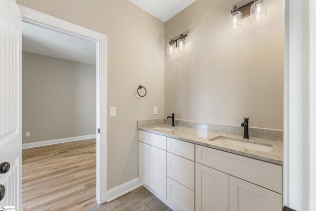 full bath featuring double vanity, wood finished floors, a sink, and baseboards