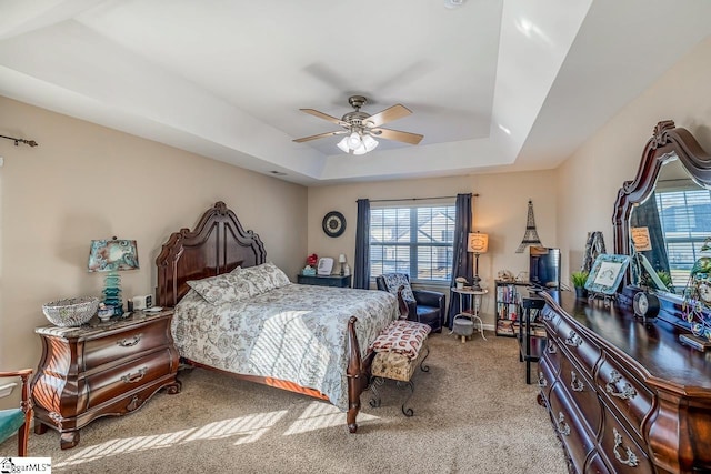 carpeted bedroom featuring a tray ceiling and ceiling fan