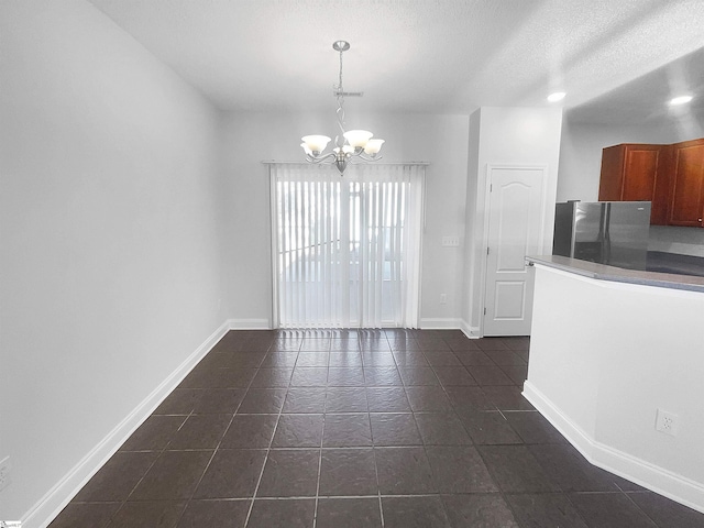 unfurnished dining area with dark tile patterned floors, a textured ceiling, and an inviting chandelier