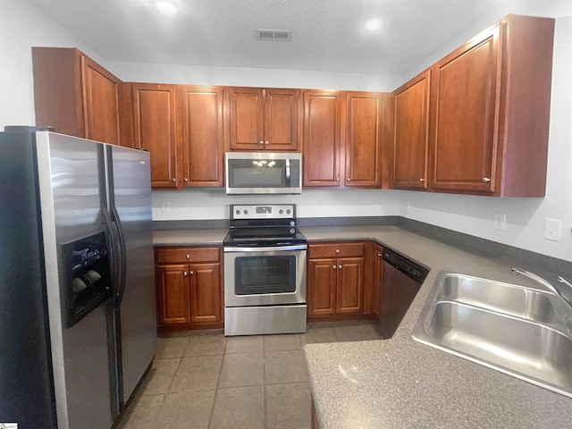 kitchen with sink, light tile patterned flooring, stainless steel appliances, and a textured ceiling