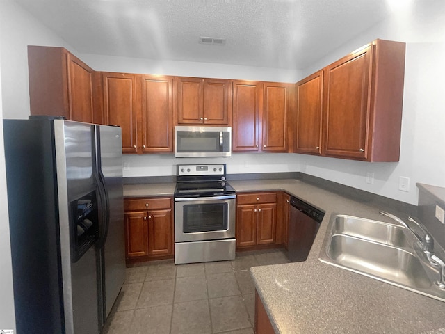 kitchen with a textured ceiling, sink, appliances with stainless steel finishes, and dark tile patterned flooring