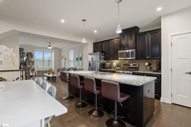 kitchen featuring stainless steel appliances, ceiling fan, a kitchen island with sink, dark hardwood / wood-style floors, and a breakfast bar area