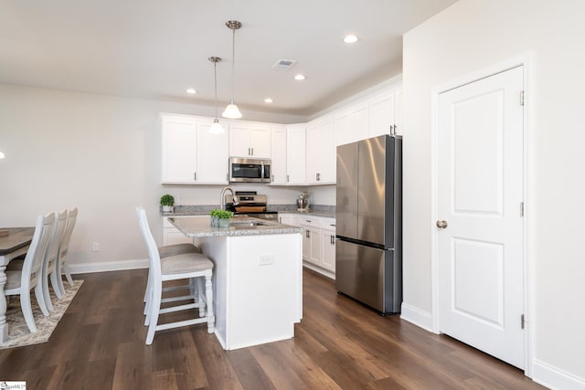 kitchen featuring white cabinets, hanging light fixtures, appliances with stainless steel finishes, and an island with sink