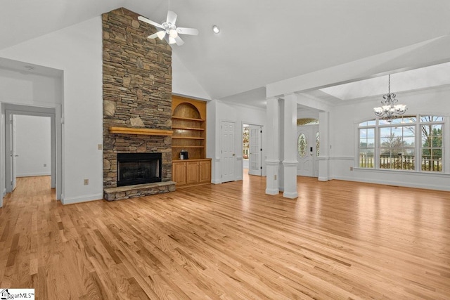 unfurnished living room featuring built in shelves, light hardwood / wood-style flooring, high vaulted ceiling, a fireplace, and ceiling fan with notable chandelier