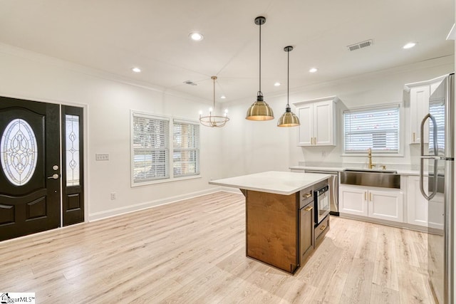 kitchen featuring sink, hanging light fixtures, a kitchen island, light hardwood / wood-style floors, and white cabinetry