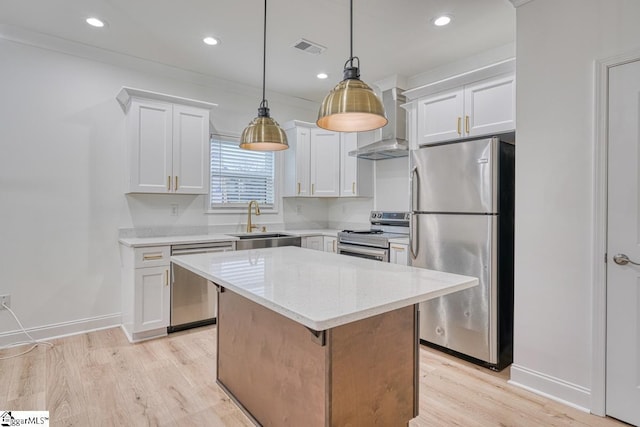 kitchen with appliances with stainless steel finishes, wall chimney range hood, sink, a center island, and white cabinetry