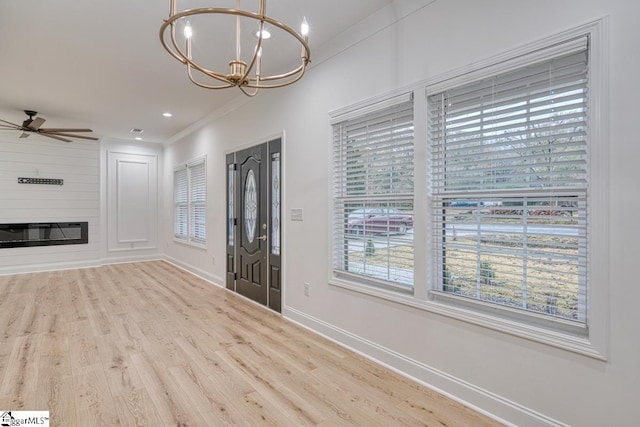 foyer with a large fireplace, light hardwood / wood-style floors, ceiling fan with notable chandelier, and ornamental molding