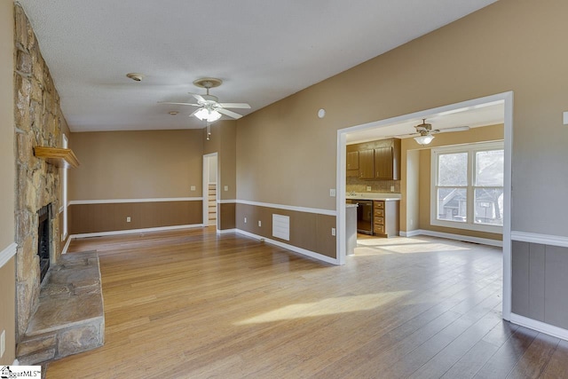 unfurnished living room with a stone fireplace, ceiling fan, light hardwood / wood-style floors, and lofted ceiling