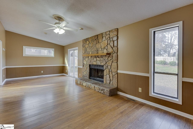 unfurnished living room with light wood-type flooring, a textured ceiling, ceiling fan, a stone fireplace, and lofted ceiling