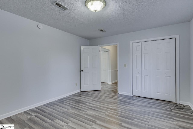 unfurnished bedroom featuring a closet, light hardwood / wood-style floors, and a textured ceiling