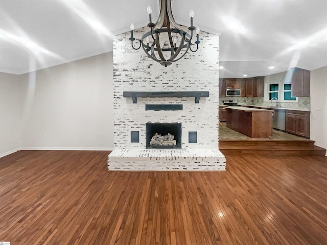 unfurnished living room with dark wood-type flooring, an inviting chandelier, sink, vaulted ceiling, and a fireplace