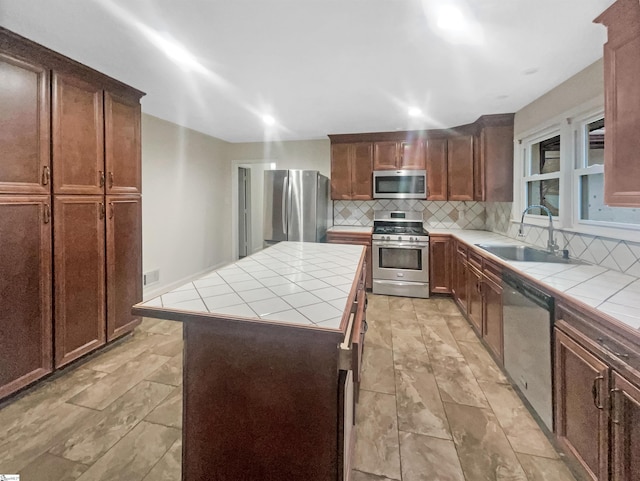 kitchen with appliances with stainless steel finishes, tile countertops, a kitchen island, and sink