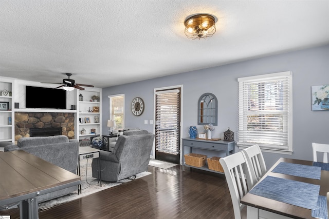 living room with a textured ceiling, a fireplace, ceiling fan, and dark wood-type flooring