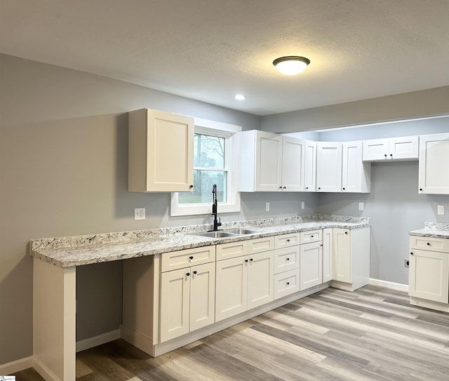 kitchen featuring white cabinets, light stone counters, light wood-type flooring, and sink