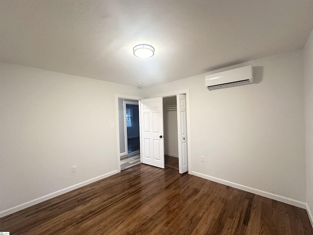 unfurnished bedroom featuring dark hardwood / wood-style floors, an AC wall unit, a textured ceiling, and a closet