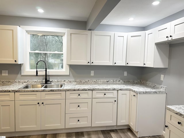 kitchen featuring white cabinets, wood-type flooring, light stone counters, and sink