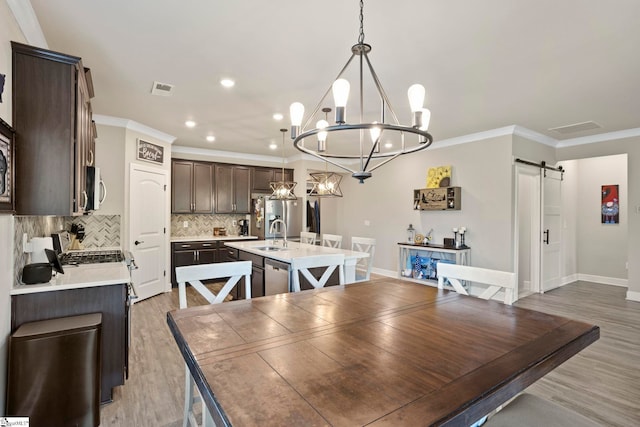 dining area featuring sink, an inviting chandelier, a barn door, crown molding, and wood-type flooring