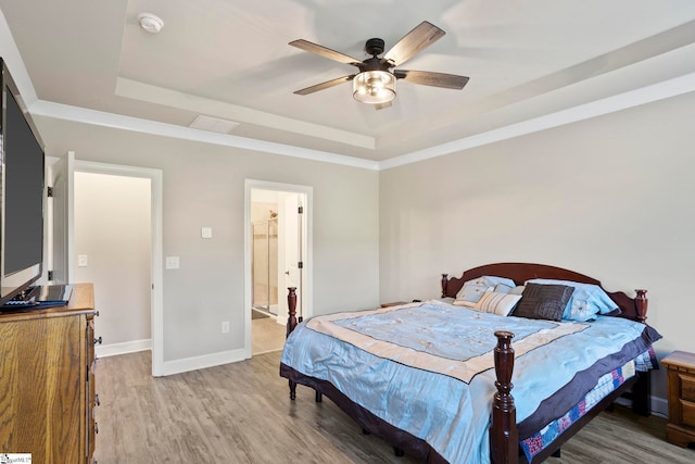 bedroom featuring a raised ceiling, ceiling fan, ensuite bathroom, and hardwood / wood-style flooring