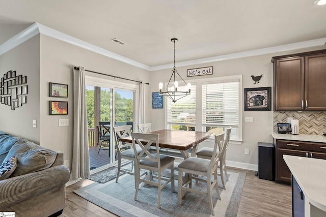 dining room with an inviting chandelier, ornamental molding, and light wood-type flooring