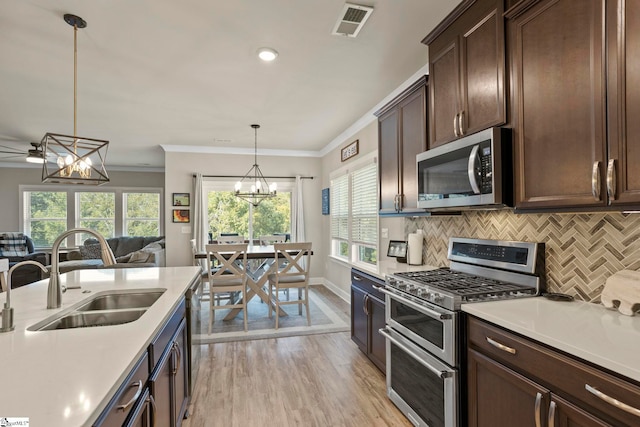 kitchen with pendant lighting, sink, light wood-type flooring, ornamental molding, and stainless steel appliances