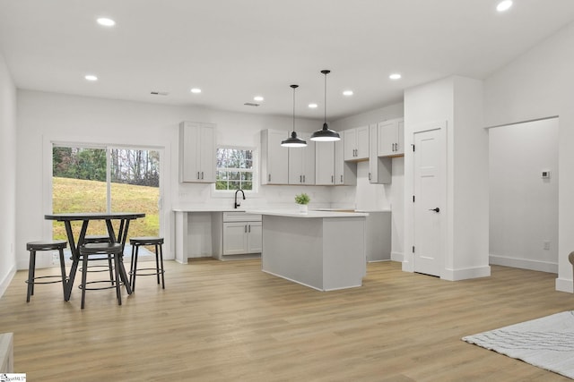 kitchen featuring light wood-type flooring, backsplash, sink, a center island, and hanging light fixtures