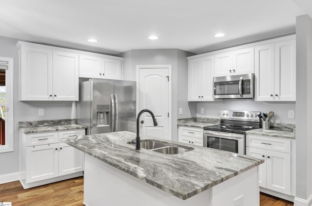 kitchen with appliances with stainless steel finishes, a kitchen island with sink, sink, white cabinets, and light hardwood / wood-style floors