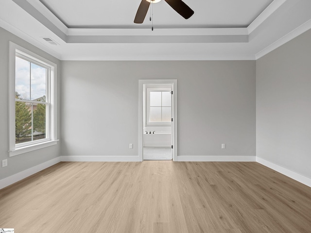 empty room with light wood-type flooring, a tray ceiling, ceiling fan, and ornamental molding