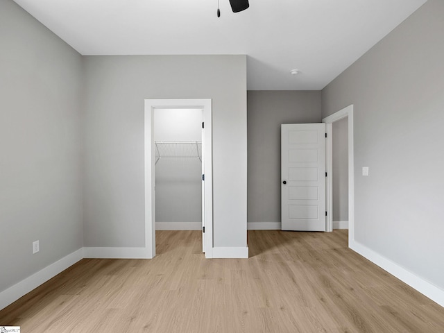 unfurnished bedroom with ceiling fan, light wood-type flooring, a spacious closet, and a closet