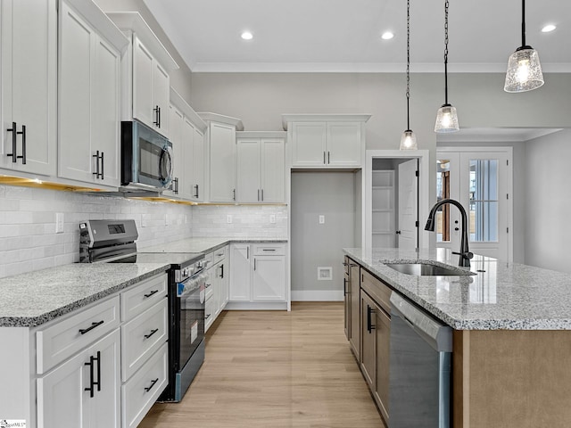 kitchen with light stone counters, stainless steel appliances, a kitchen island with sink, sink, and white cabinets