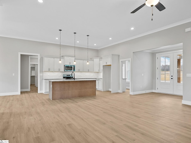 kitchen featuring a center island with sink, white cabinets, hanging light fixtures, light wood-type flooring, and appliances with stainless steel finishes