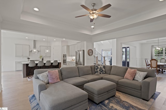 living room featuring light hardwood / wood-style floors, a raised ceiling, ceiling fan, and ornamental molding