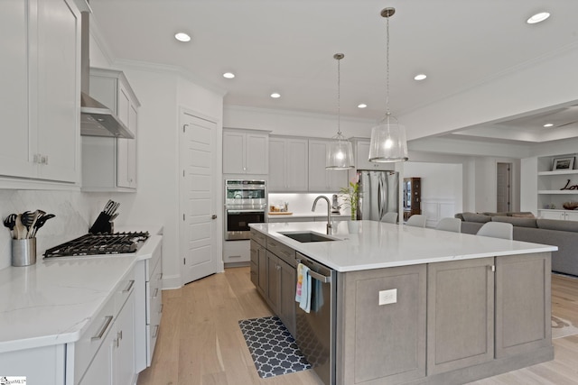 kitchen with a large island, sink, decorative light fixtures, appliances with stainless steel finishes, and light wood-type flooring