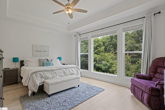 bedroom featuring light hardwood / wood-style floors, ceiling fan, ornamental molding, and a tray ceiling