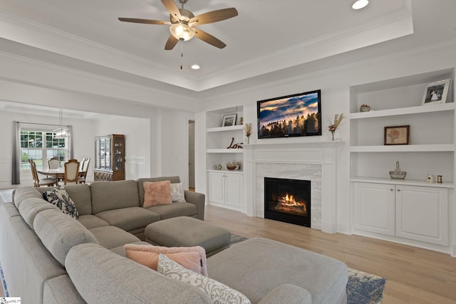 living room featuring crown molding, light hardwood / wood-style flooring, ceiling fan, built in features, and a fireplace