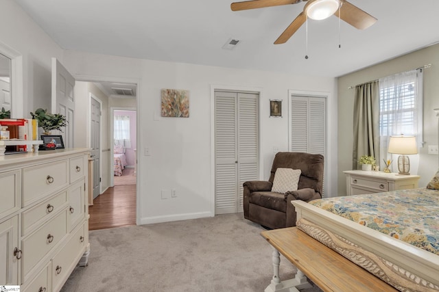 bedroom featuring multiple windows, ceiling fan, light colored carpet, and multiple closets