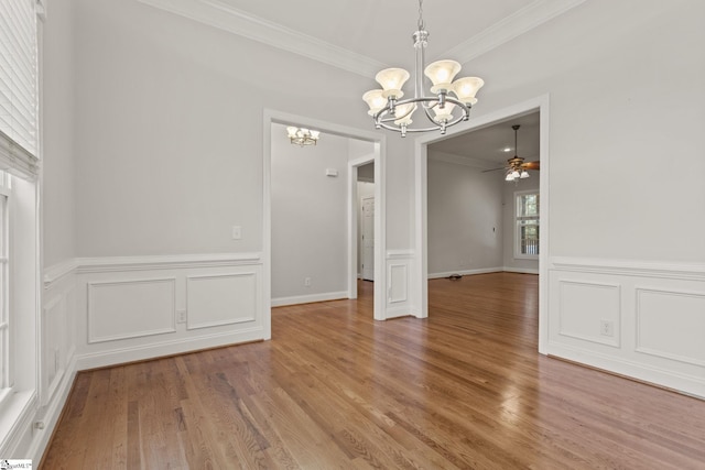 unfurnished dining area featuring wood-type flooring, ceiling fan with notable chandelier, and ornamental molding