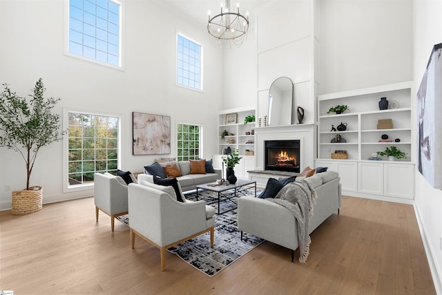 living room with an inviting chandelier, a towering ceiling, and light wood-type flooring