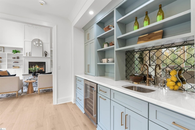 bar featuring wine cooler, light stone countertops, sink, and light wood-type flooring