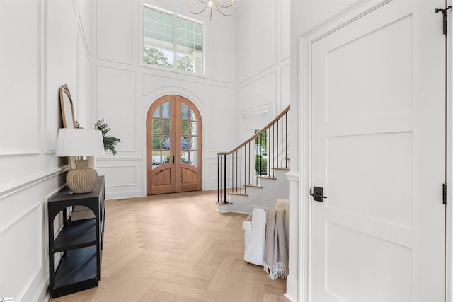 entrance foyer featuring light parquet flooring, an inviting chandelier, and french doors