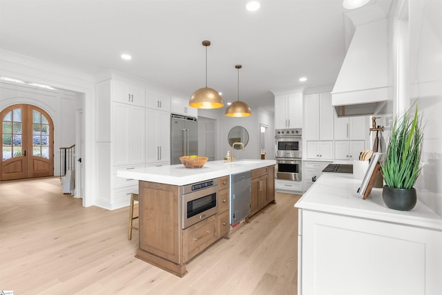 kitchen with french doors, stainless steel appliances, a center island with sink, white cabinets, and hanging light fixtures