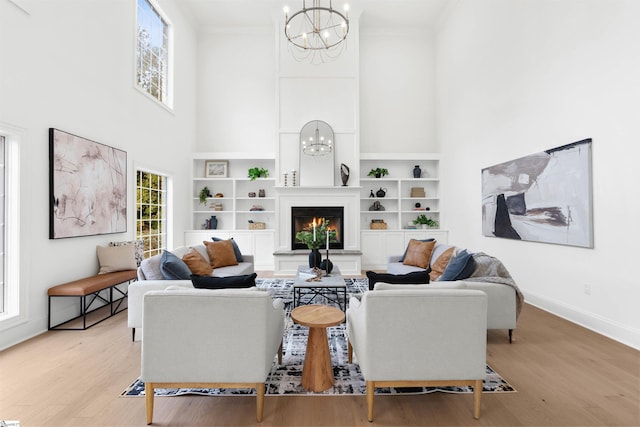 living room featuring an inviting chandelier, ornamental molding, a high ceiling, and light hardwood / wood-style flooring