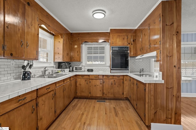 kitchen featuring black appliances, decorative backsplash, ornamental molding, and light hardwood / wood-style flooring