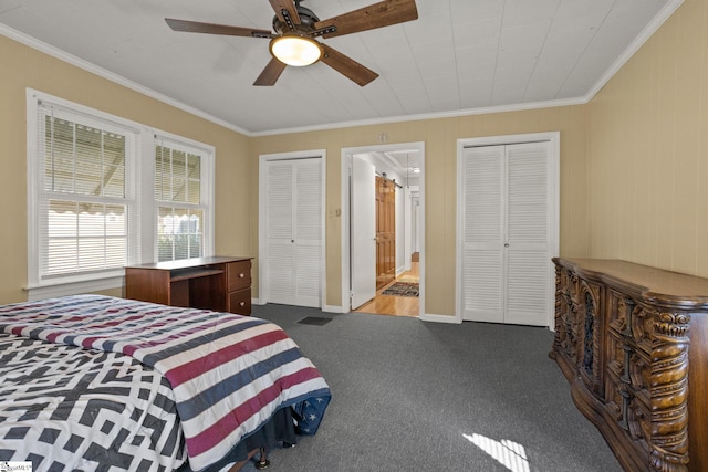 carpeted bedroom featuring ceiling fan, ornamental molding, ensuite bathroom, and two closets