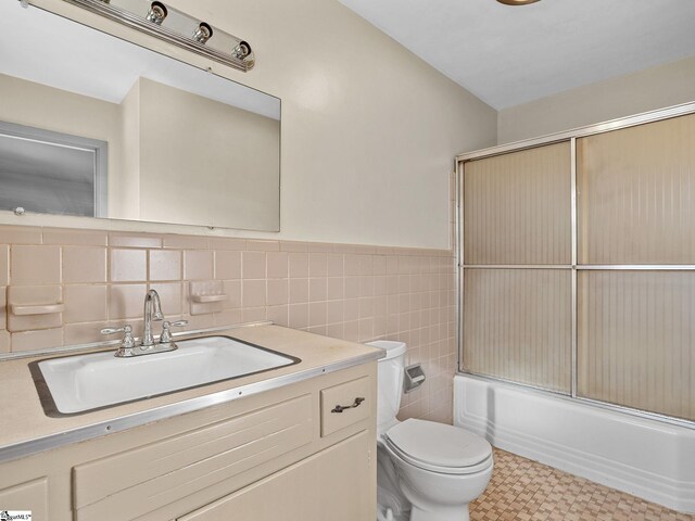 full bathroom featuring toilet, vanity, tile walls, and combined bath / shower with glass door