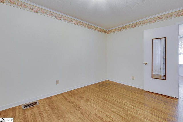 empty room featuring a textured ceiling, light wood-type flooring, and ornamental molding