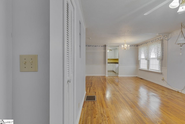 unfurnished bedroom with ceiling fan with notable chandelier, light wood-type flooring, and a textured ceiling